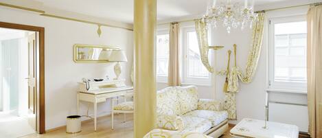 A spacious room with a large window, a white desk with a telephone, a sofa, and a small table.
