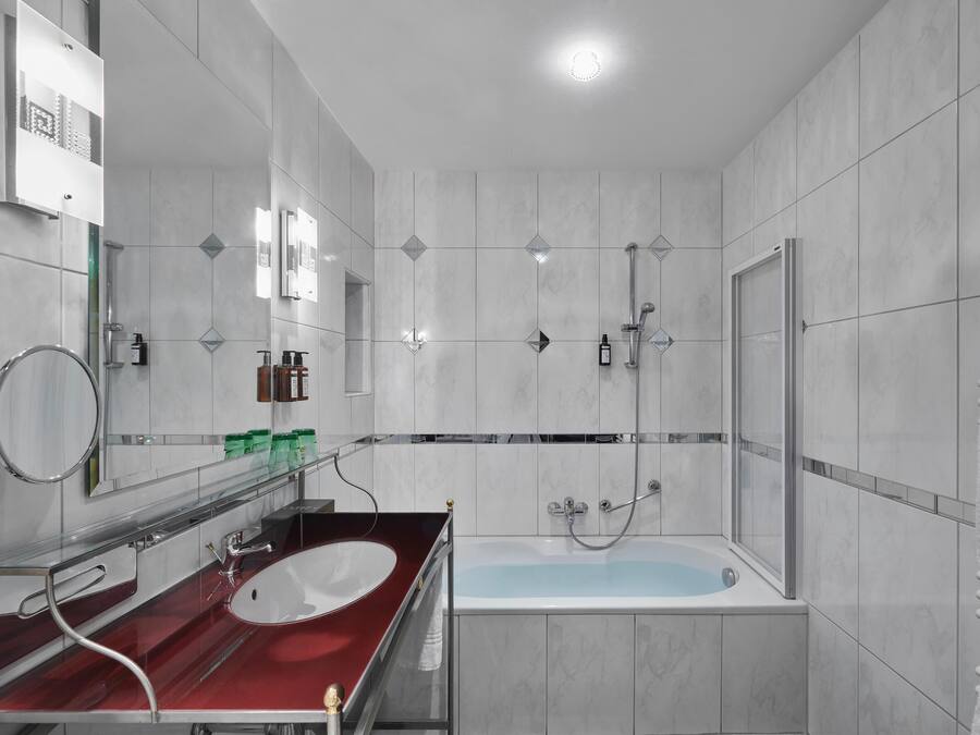 A modern bathroom with a red vanity, a white bathtub, and a glass shower enclosure.