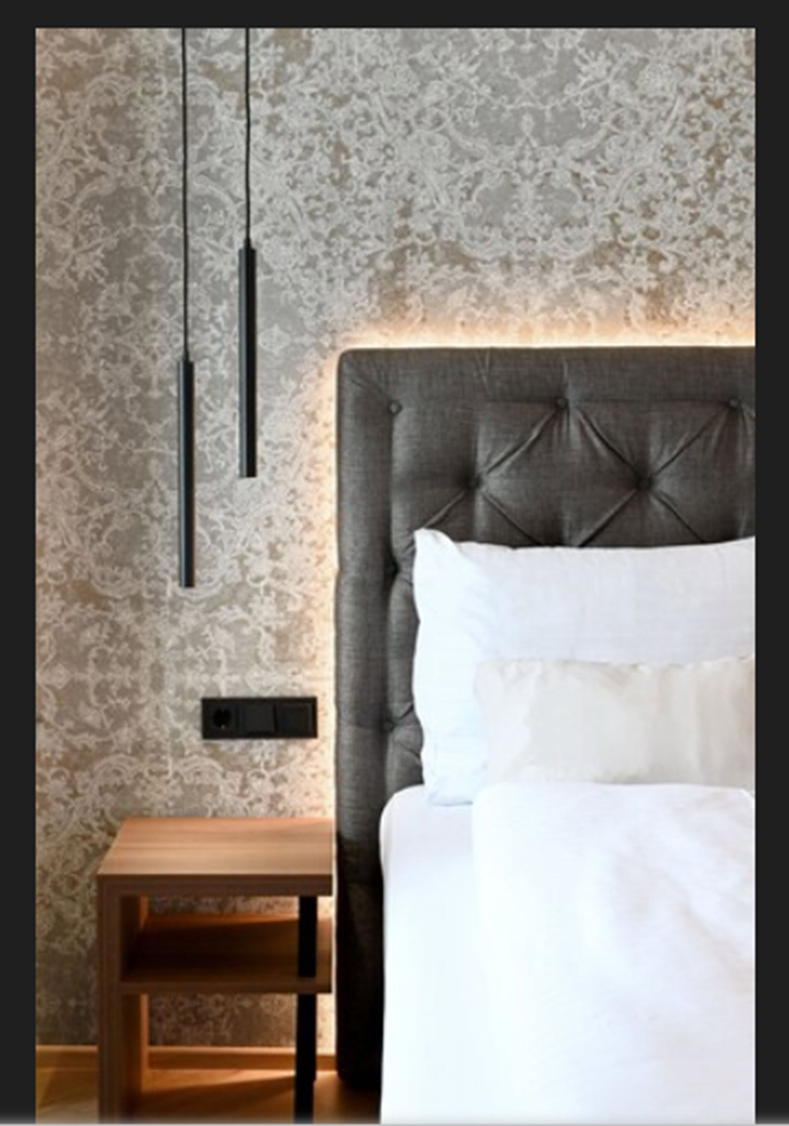 Un dormitorio con cabecera capitonada, una mesita de noche y una lámpara de pared.