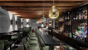 A bar area with green bar stools, a long counter, and a variety of liquor bottles. - Hotel Schwarzer Adler (Innsbruck)