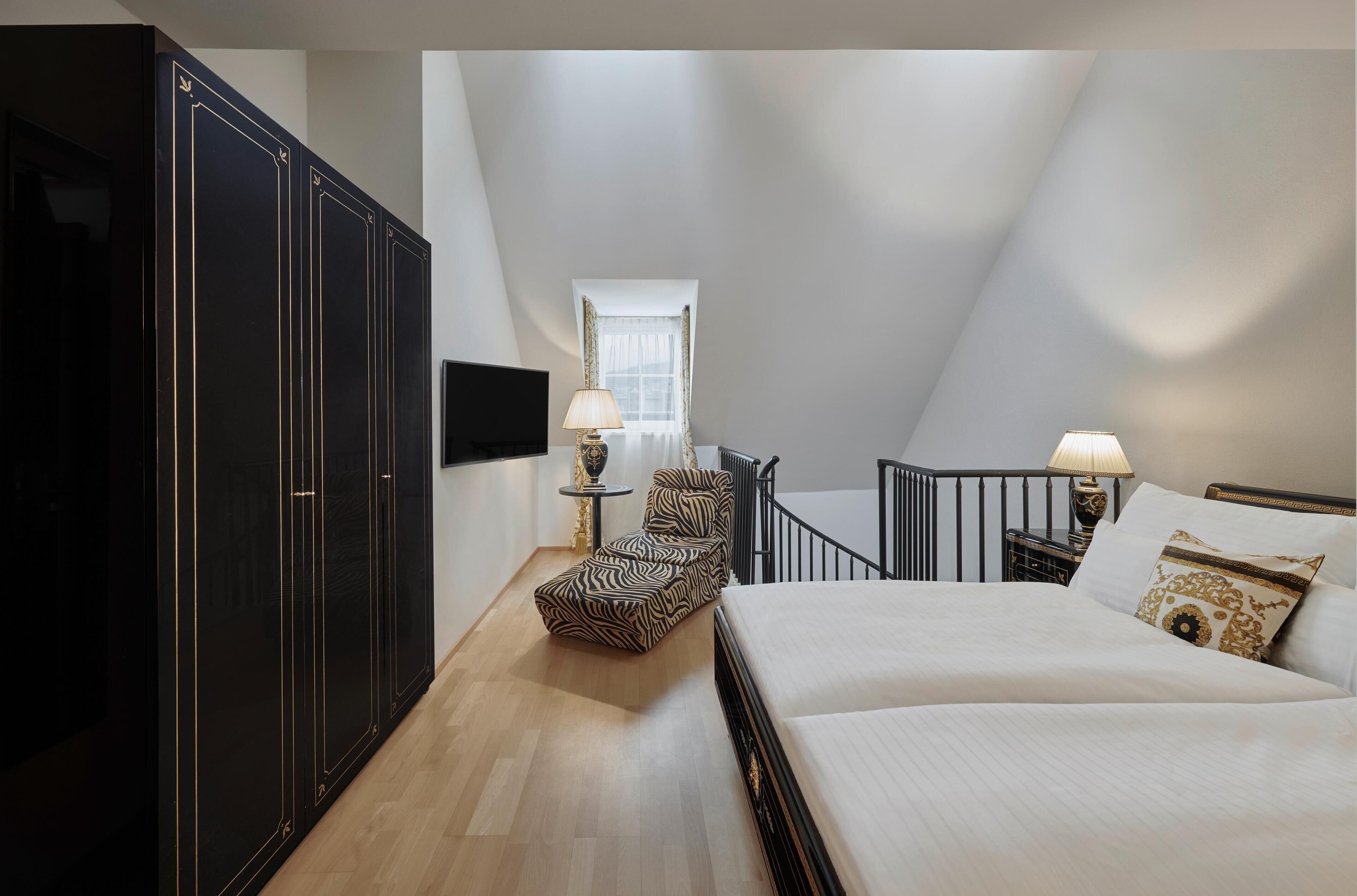 A bedroom with a bed, a chair, a wardrobe, a TV, and a window.