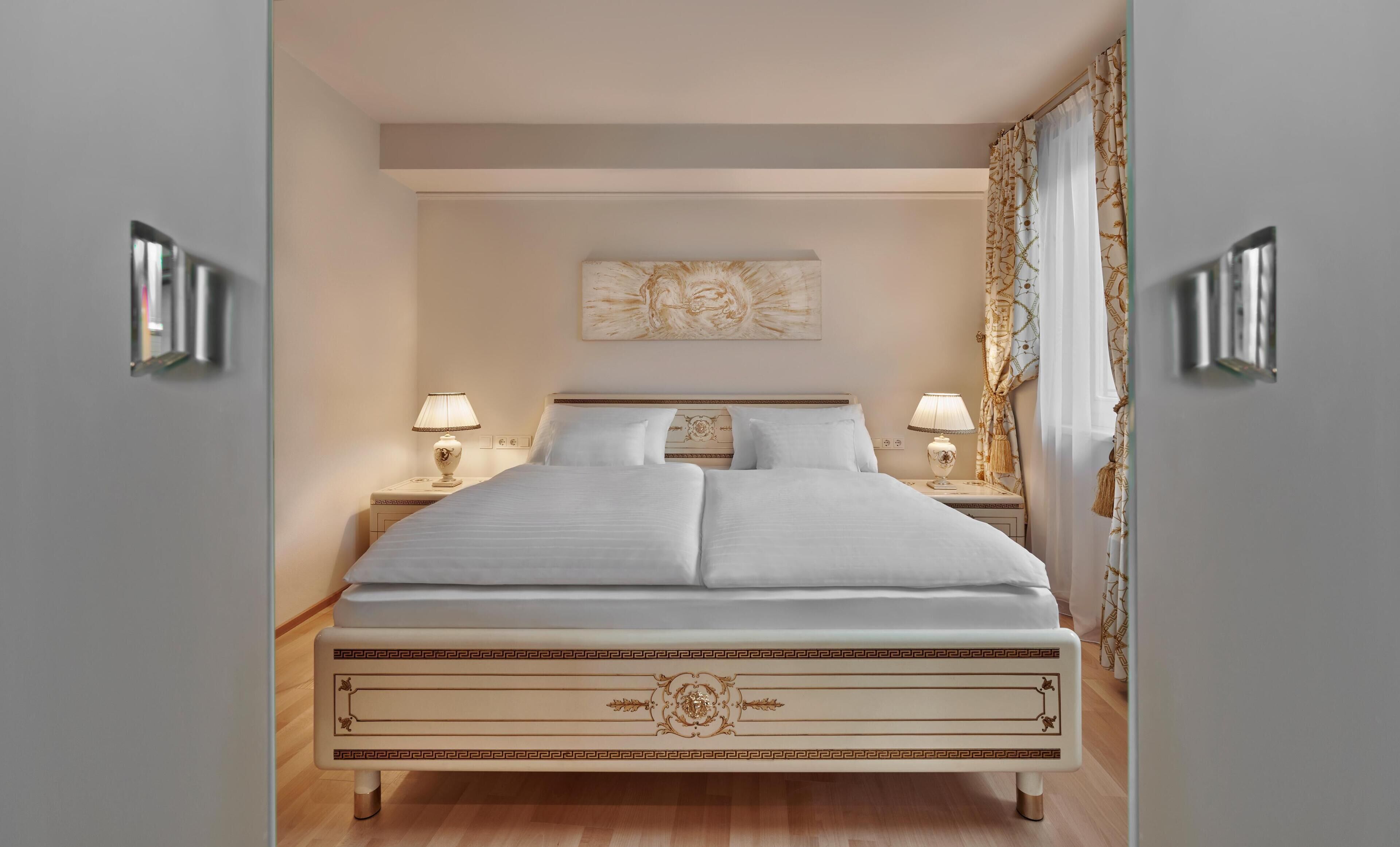 A neatly made bed with a decorative headboard, two bedside lamps, and a wall-mounted artwork above.