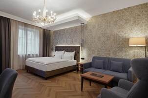 Habitación de hotel con una cama grande, un sofá, una mesa de centro y un candelabro.