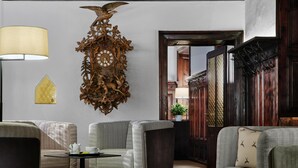 A cozy living room with a large wooden clock, a lamp, and two sofas. - Hotel Schwarzer Adler (Innsbruck)