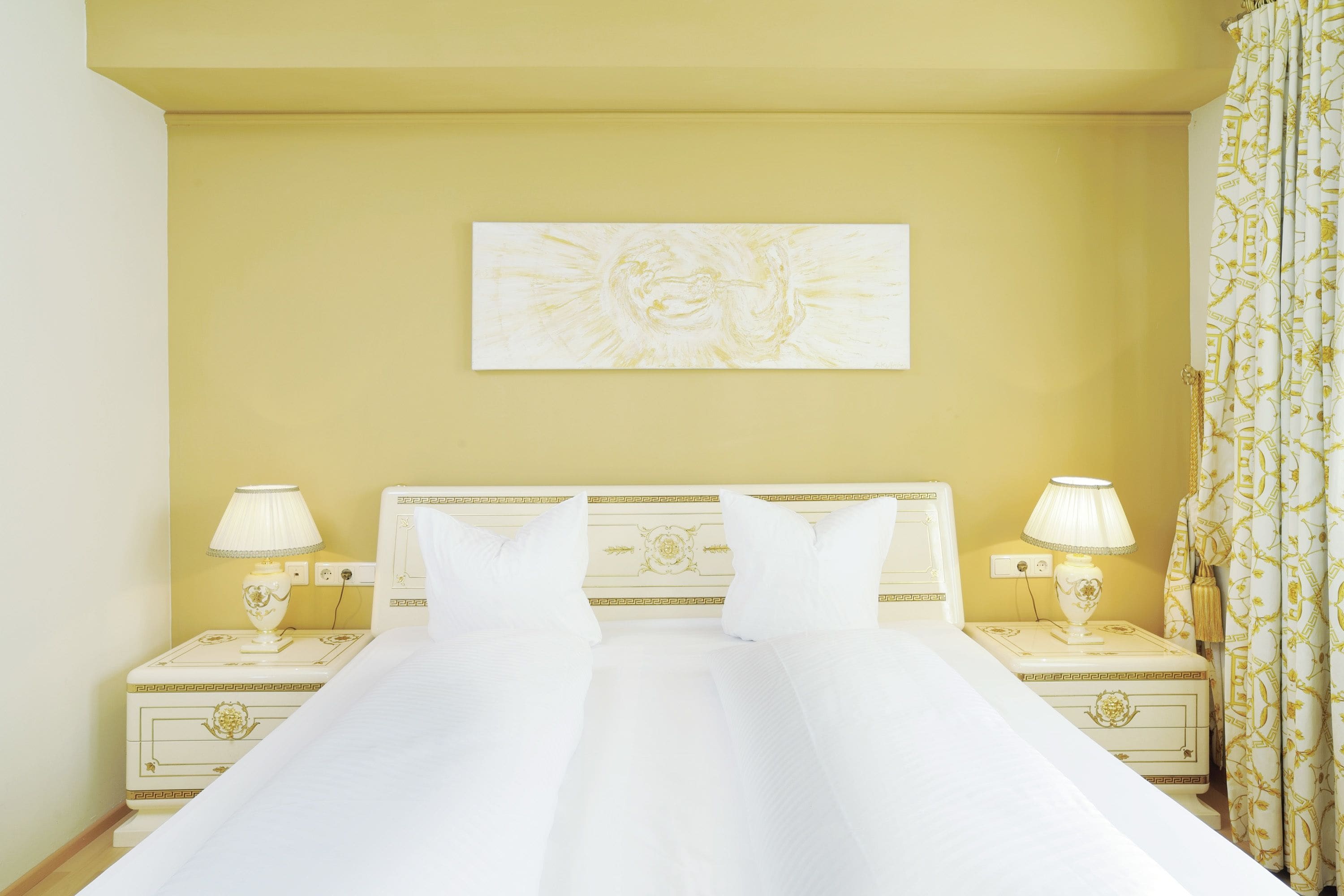 Ein Hotelzimmer mit einem großen Bett, zwei Nachttischen mit Lampen, einer dekorativen Kopfteil und einem Bild an der Wand.