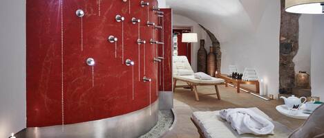 A spa room with a red wall, a massage table, a lounge chair, and a tea set.