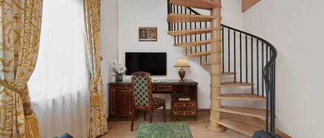 A living room with a wooden spiral staircase, a desk with a computer, a chair, and a sofa with patterned cushions.