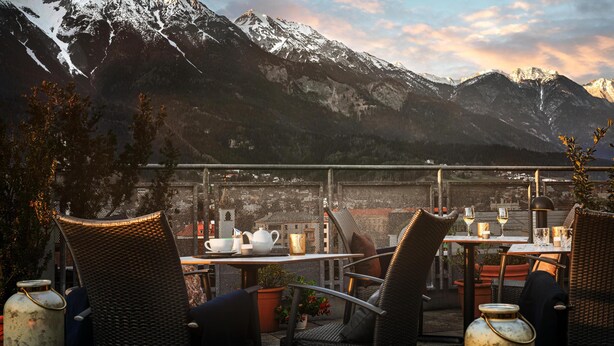 A terrace with wicker chairs and tables, overlooking a mountainous landscape with snow-capped peaks. - Hotel Schwarzer Adler (Innsbruck)