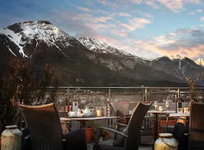 A terrace with wicker chairs and tables, overlooking a mountainous landscape with snow-capped peaks. - Hotel Schwarzer Adler (Innsbruck)