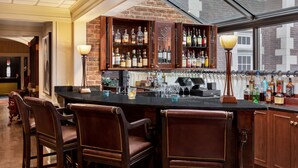 A bar area with wooden cabinets, bar stools, and a variety of bottles. - The Glidden House (Cleveland)
