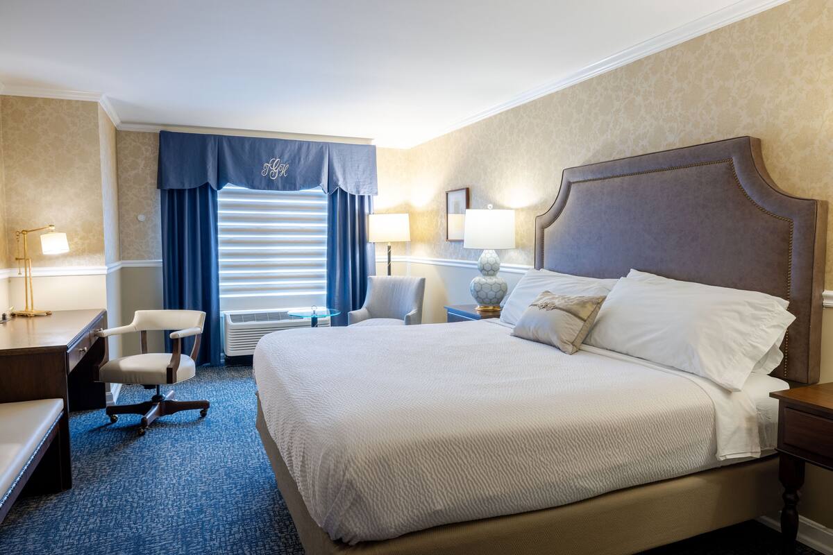 A hotel room with a large bed, a desk, a chair, and a window with curtains.