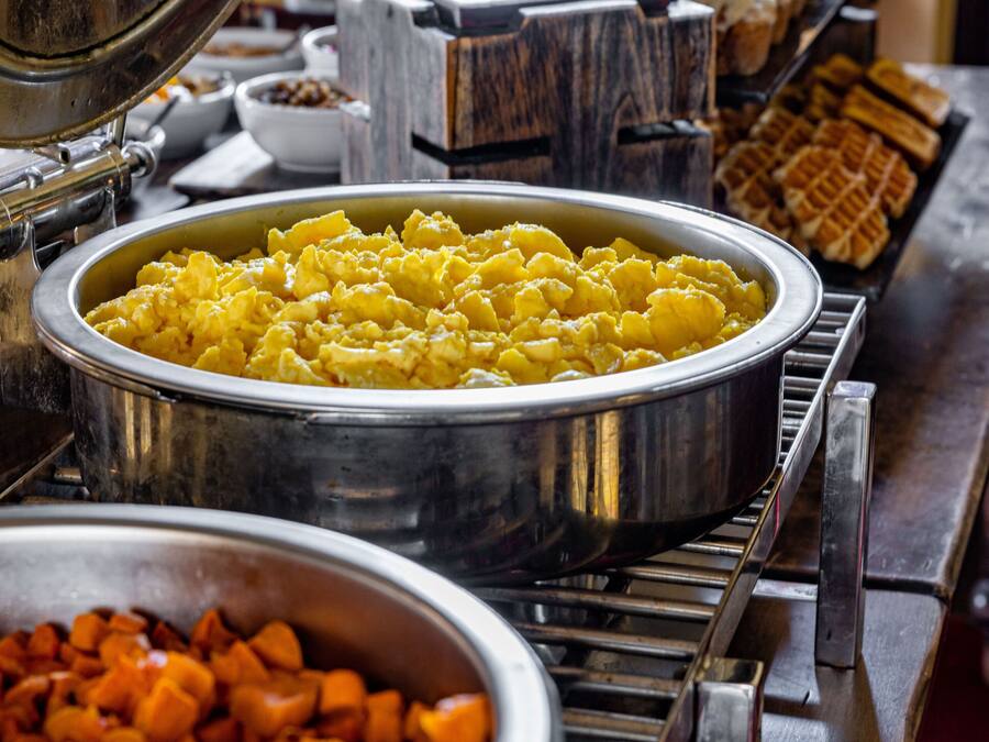 A buffet with various food items including scrambled eggs, waffles, and a large bowl of fruit.
