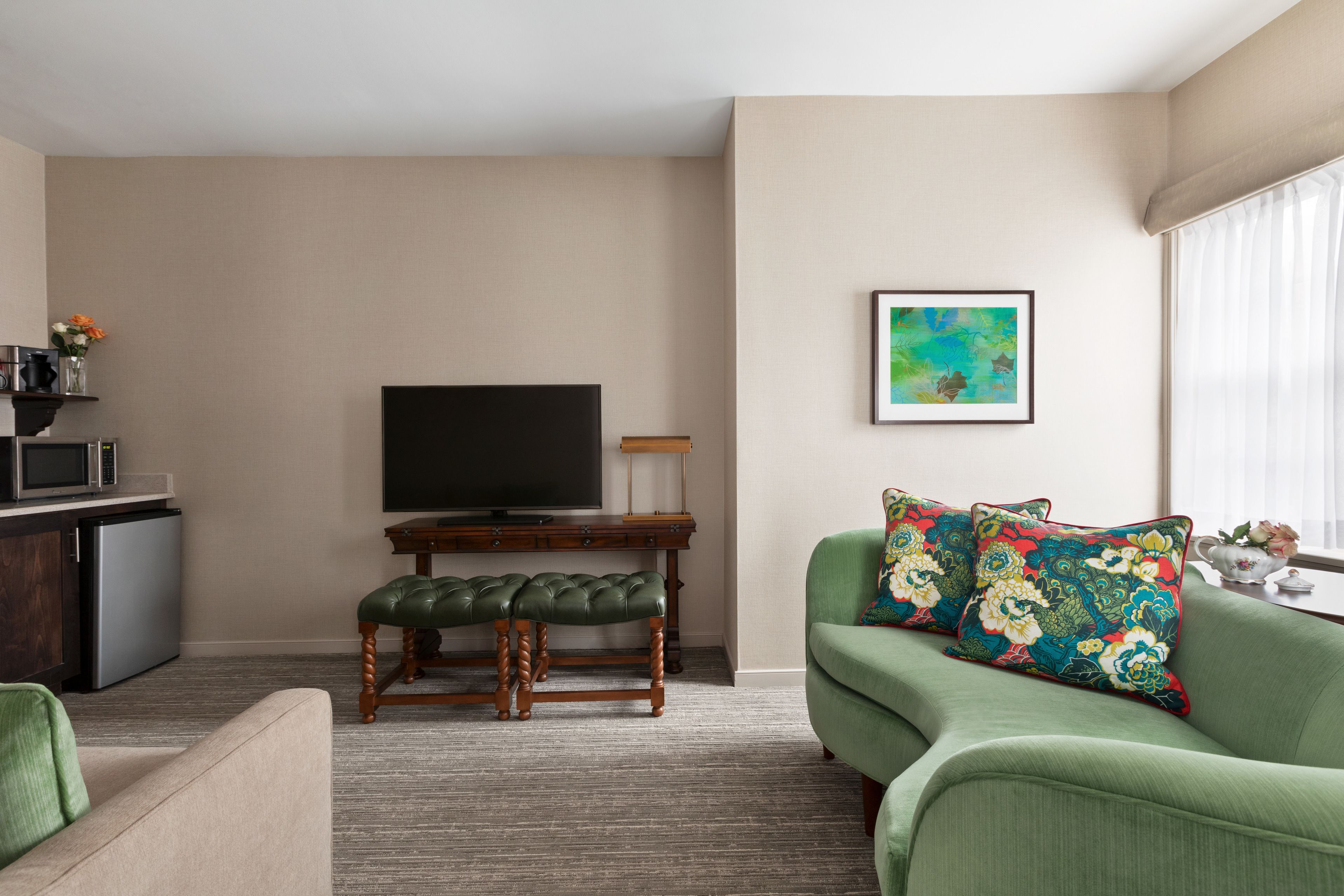 A living room with a green sofa, a wooden bench, a flat-screen TV, a small table, and a framed artwork on the wall.
