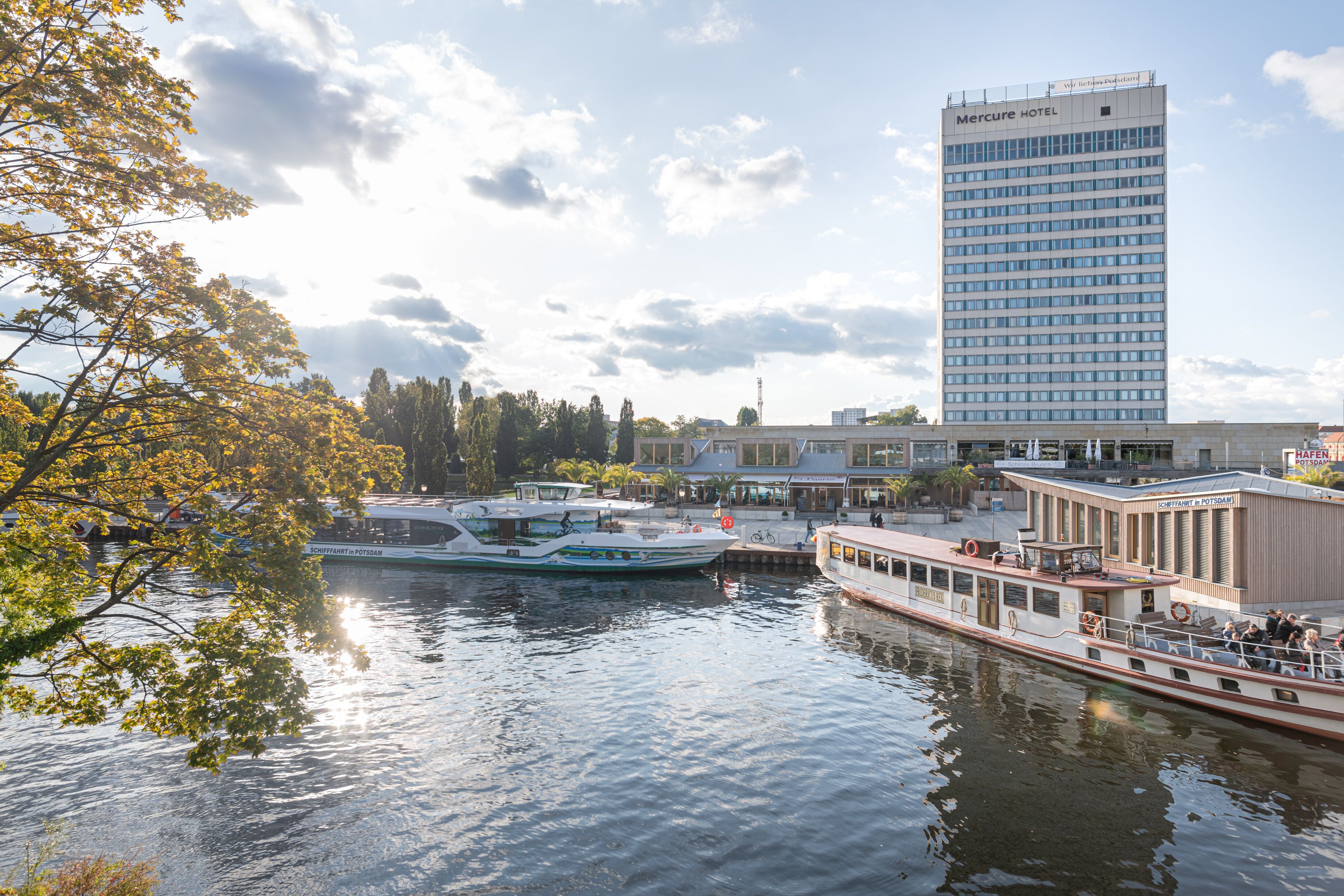 A riverfront view with a hotel, boats, and a building with a sign reading "Mercure HOTEL".
