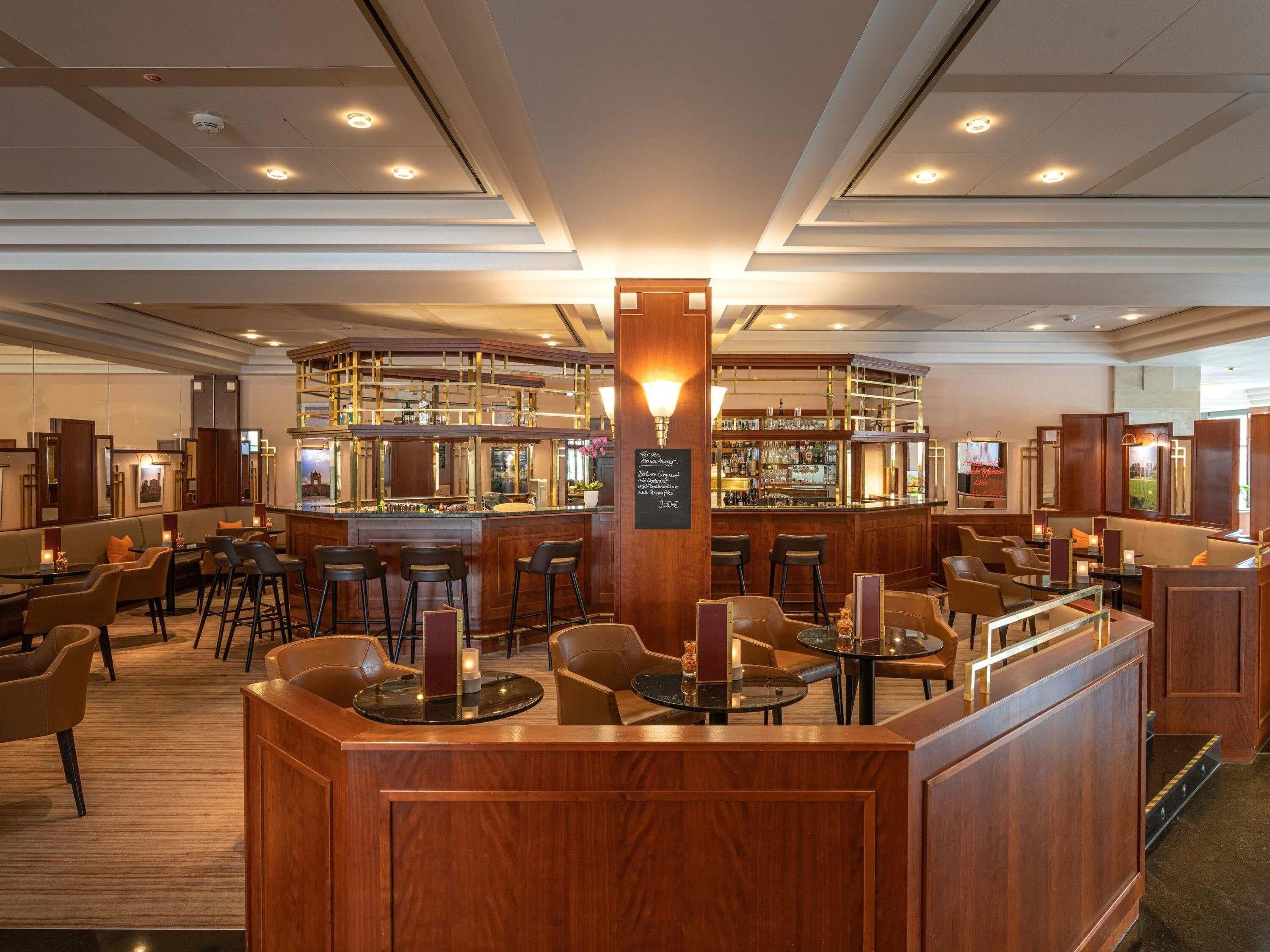 Zona de bar con mostrador de madera, diversas opciones de asientos, incluyendo taburetes y mesas, y un cartel de menú visible.