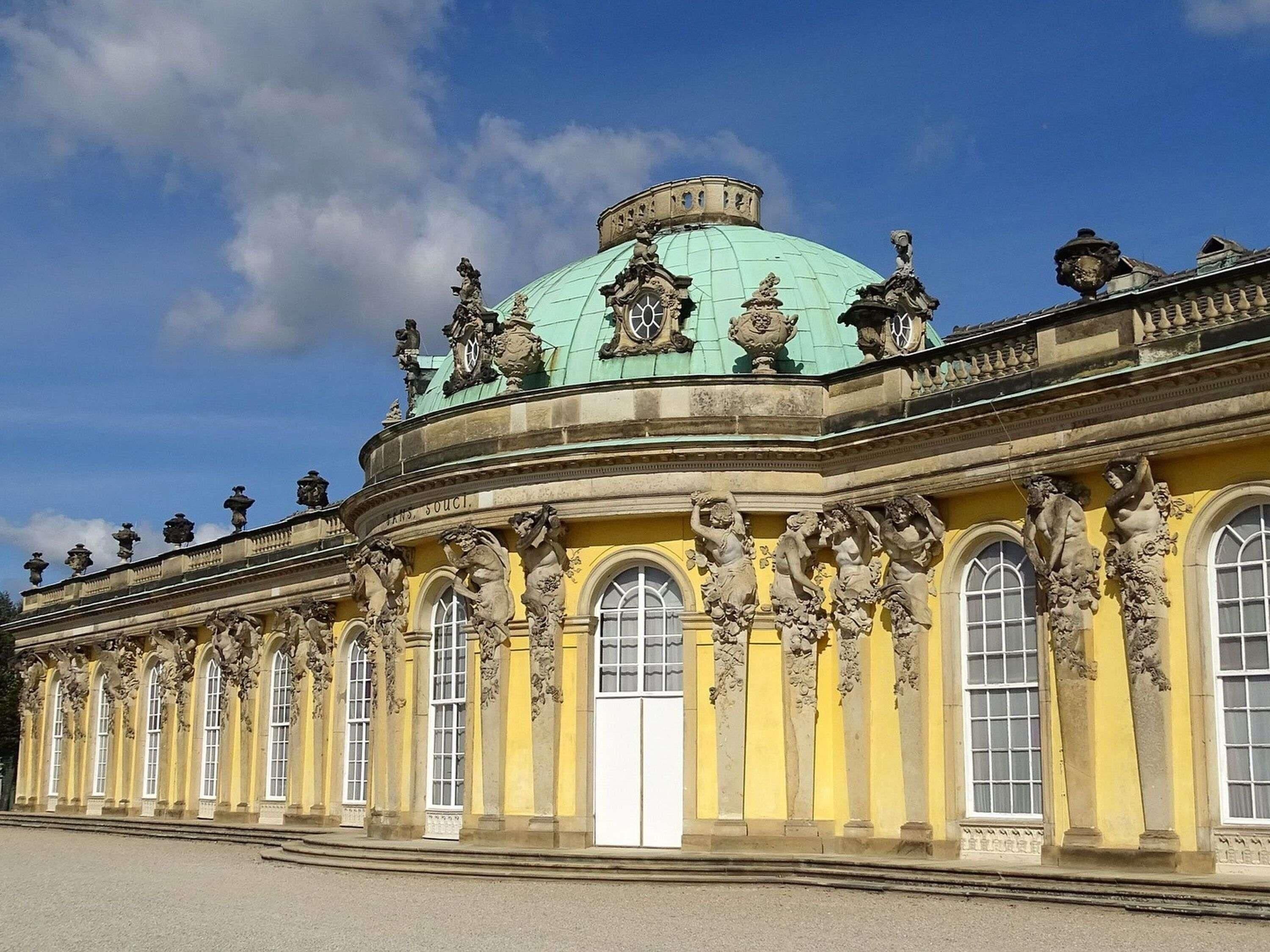 A classical building with a green dome, ornate sculptures, and a yellow facade.