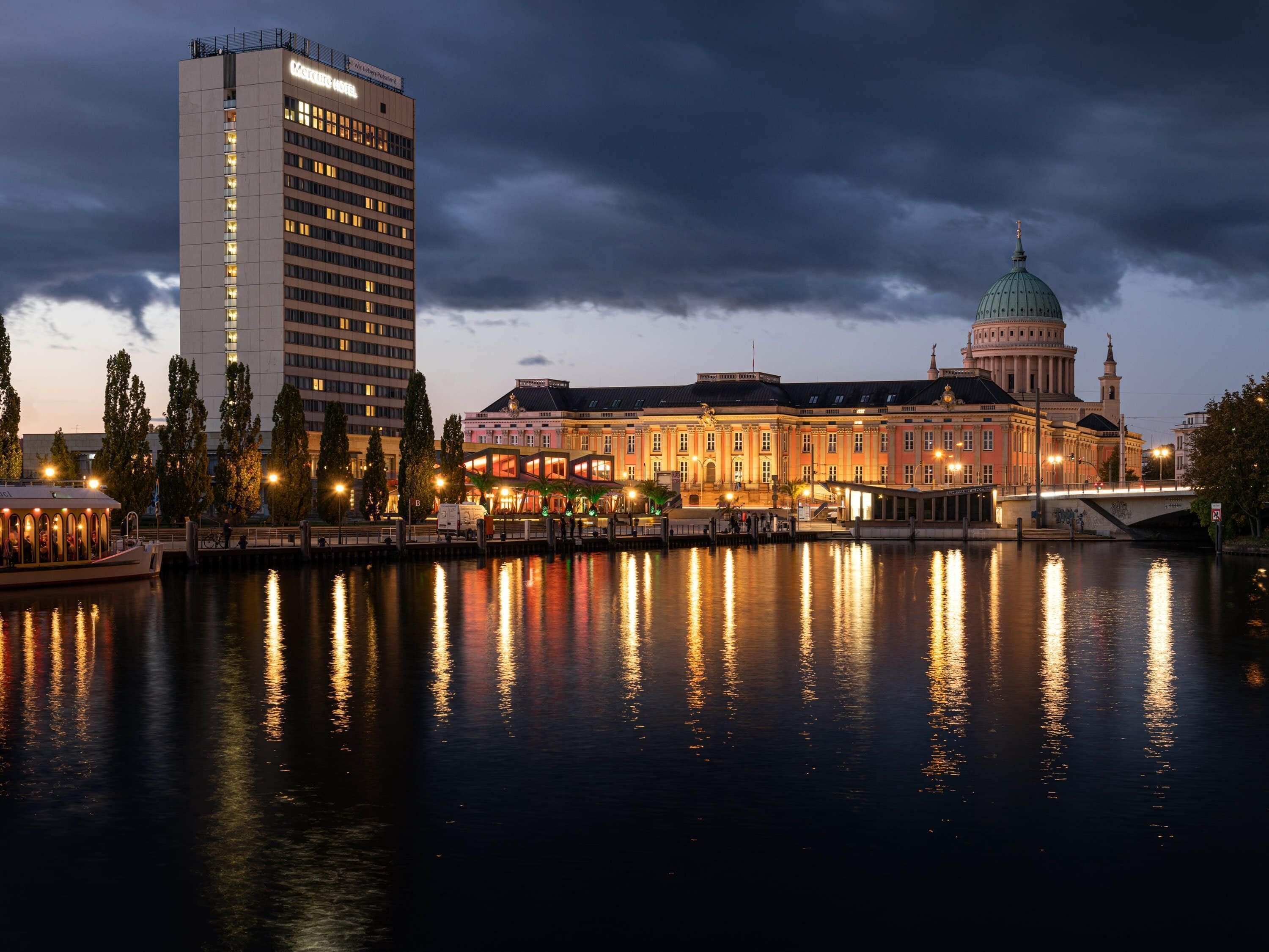 Ein historisches Gebäude mit einer Kuppel, ein modernes Hotel und ein Fluss, der die Bauten widerspiegelt.
