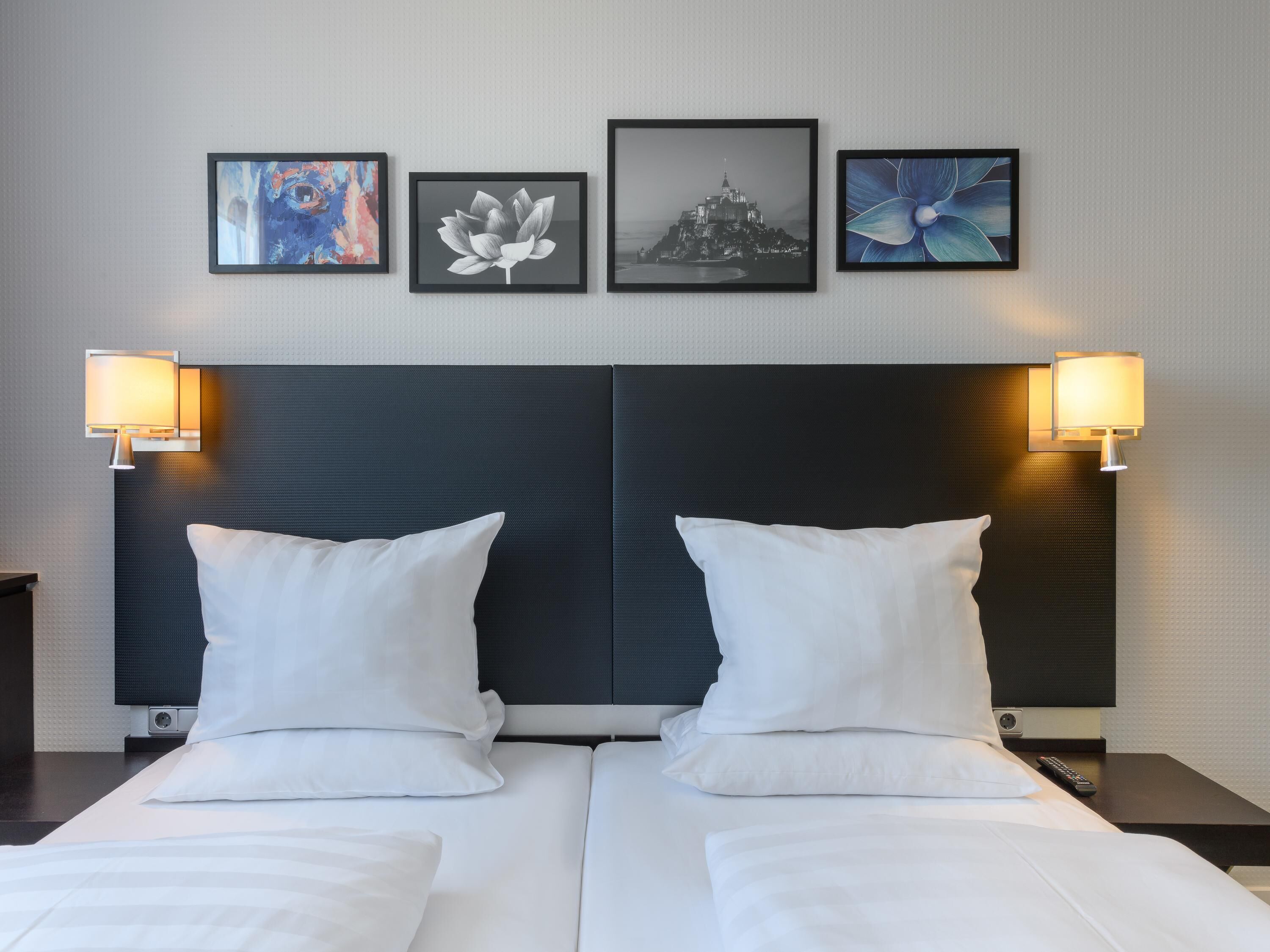 Ein Hotelzimmer mit einem großen Bett, zwei Nachttischlampen und vier gerahmten Kunstwerken an der Wand.