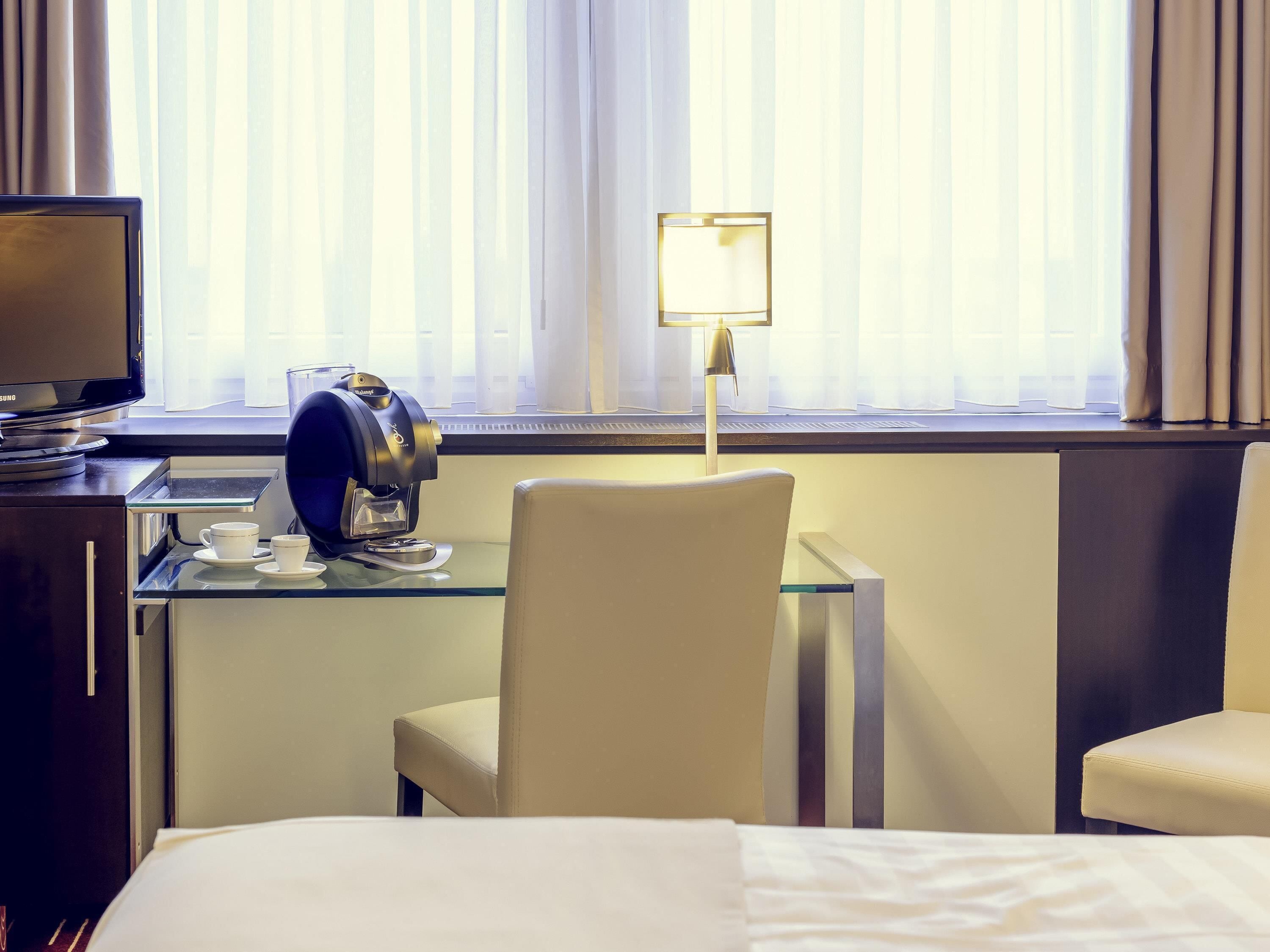 Una habitación de hotel con cama, escritorio con cafetera, lámpara y televisor.