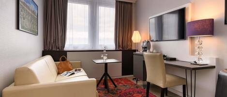 Habitación de hotel con sofá, escritorio, silla, televisor y lámpara.