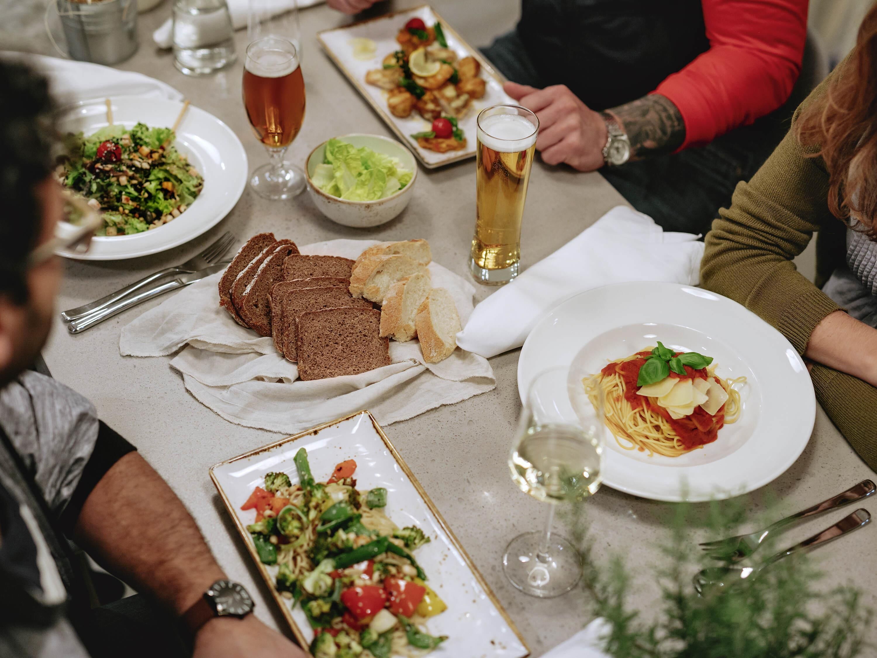 Uma mesa de jantar com diversos pratos, incluindo massa, pão e salada.