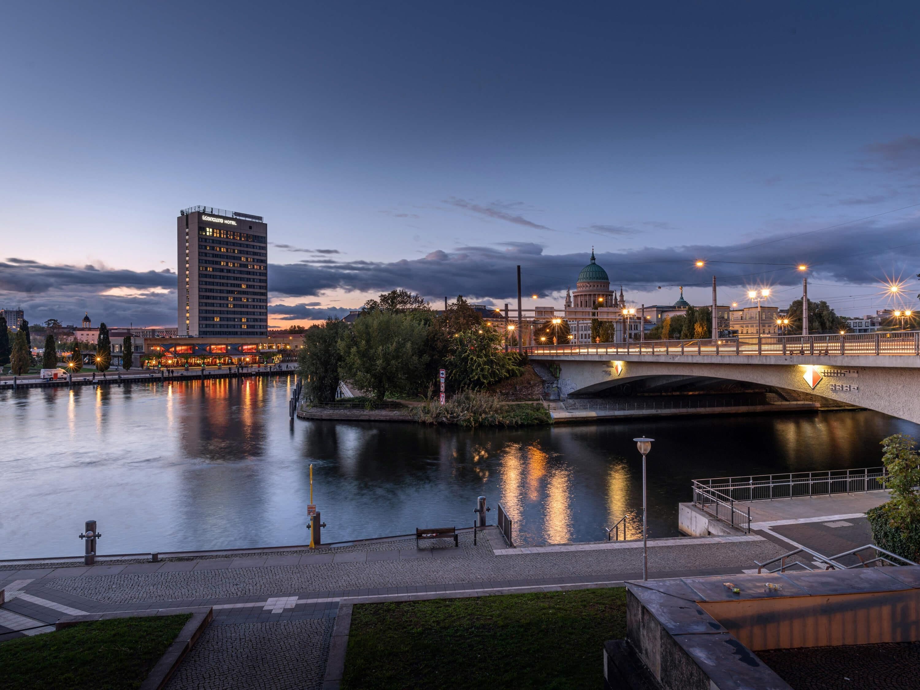 A riverside view with a bridge, a large building with a dome, and a hotel with a lit facade.