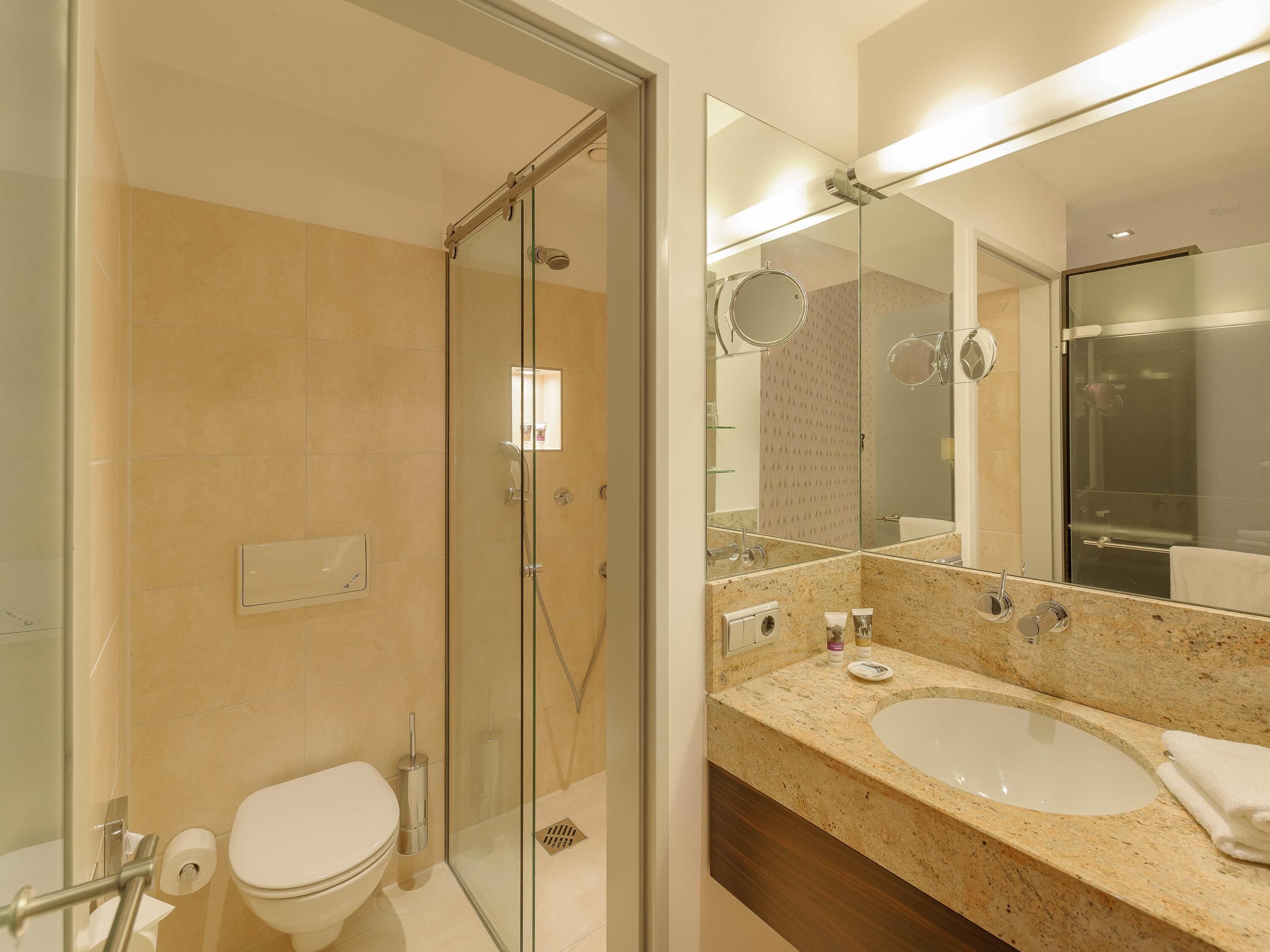 Un baño con ducha de vidrio, inodoro blanco, lavabo con espejo y una toalla.