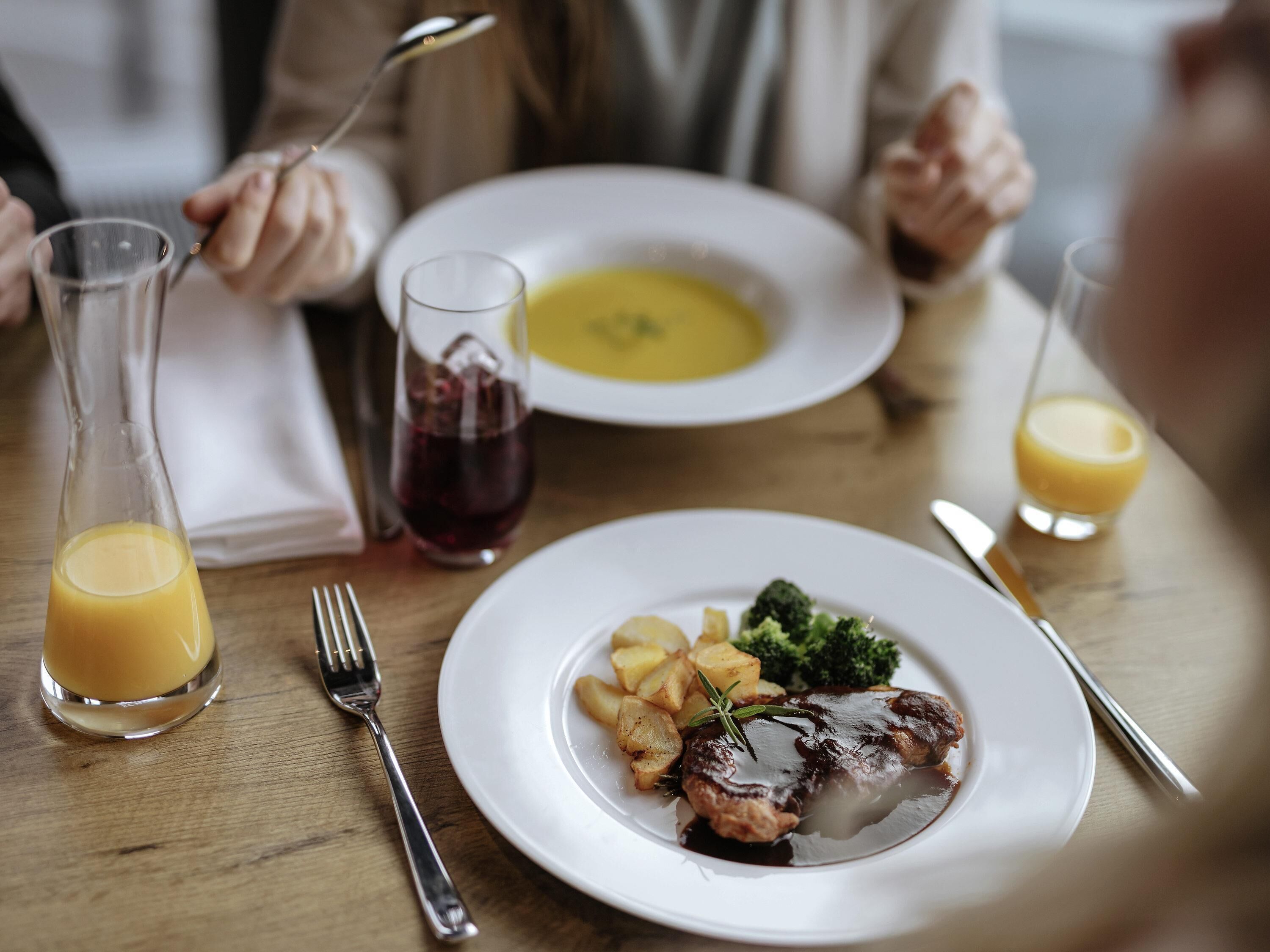 A dining table with a plate of food, a glass of juice, and a glass of red wine.