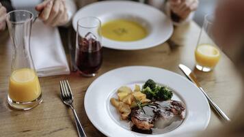 A dining table with a plate of food, a glass of juice, and a glass of red wine.
