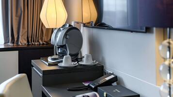 A hotel room with a coffee machine, a remote control, a magazine, a smartphone, and a TV on the wall.