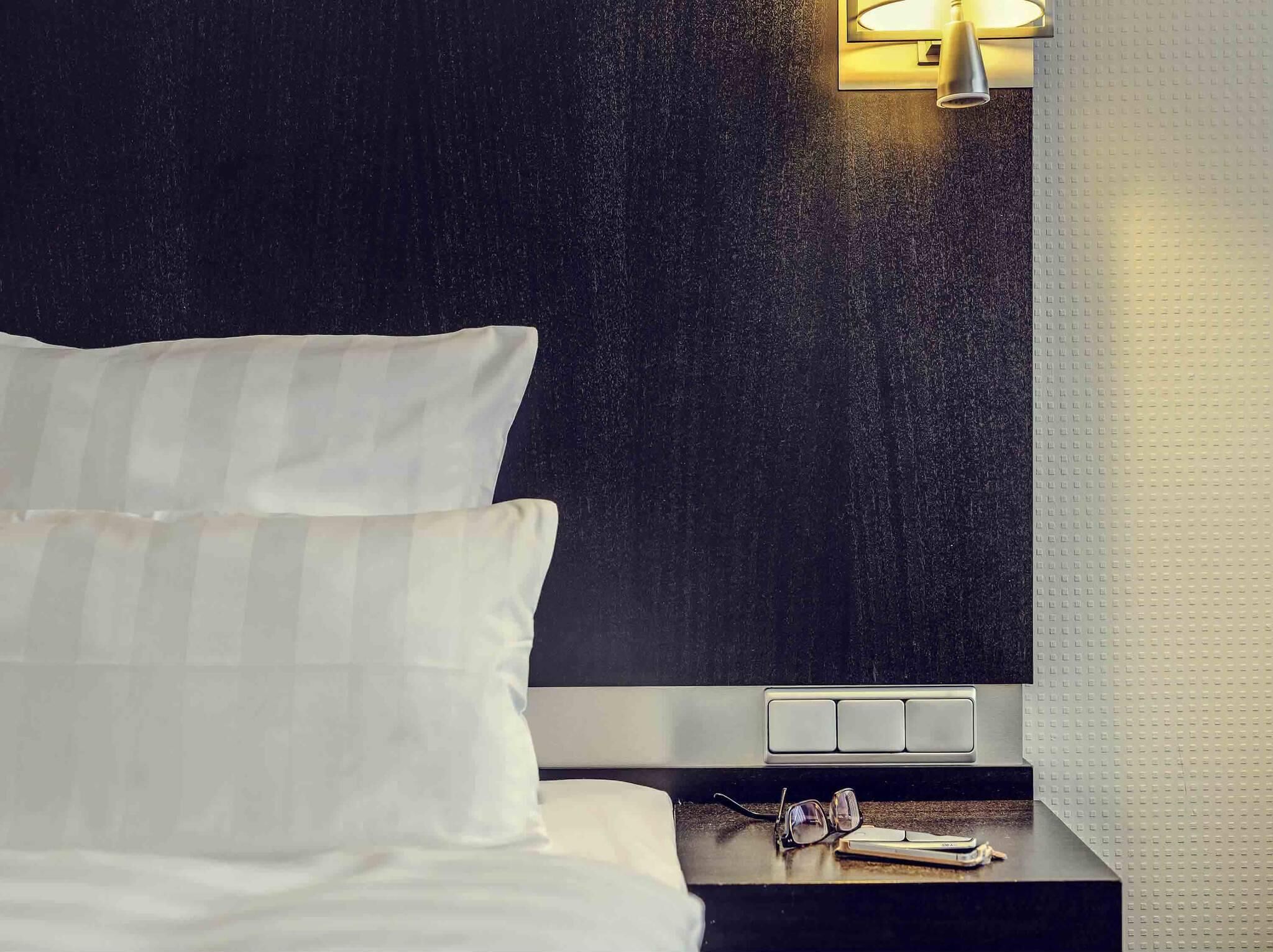A bed with white linens, a nightstand with a lamp, and a wall with a textured pattern.