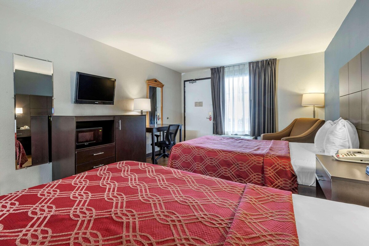 A hotel room with two beds, a desk with a chair, a TV mounted on the wall, and a bathroom door.
