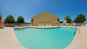 Una piscina de borde curvo, rodeada por una valla blanca, y un edificio con techo plano al fondo.