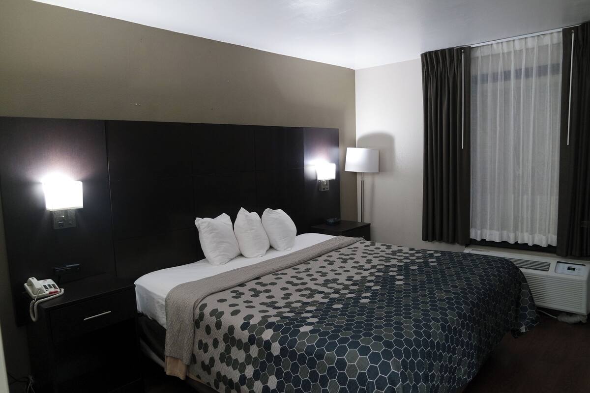 A hotel room with a bed, bedside lamps, a phone, and a window with curtains.