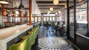 L’intérieur d’un restaurant avec un bar, des chaises vertes, un sol à motifs et de grandes fenêtres.