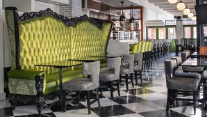 Un restaurant avec un sol à carreaux, des sièges recouverts d’un tissu vert et un coin bar.