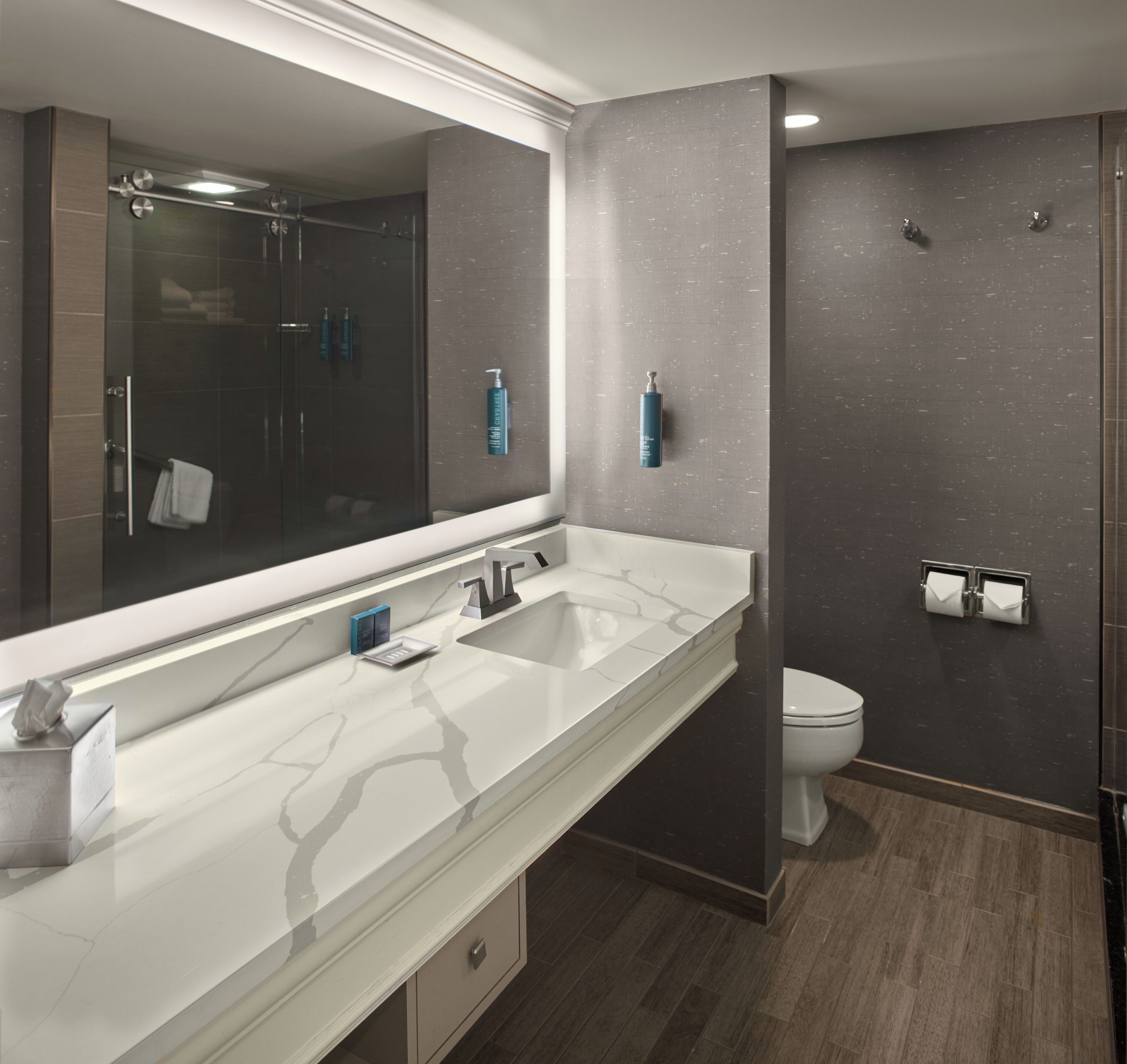 A modern bathroom with a large mirror, dual sinks, a toilet, and a shower area.