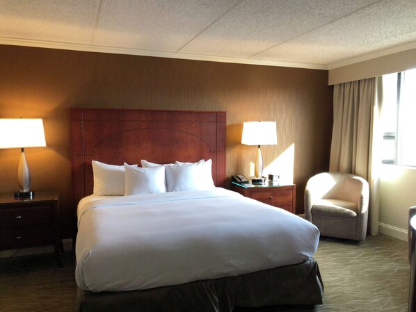 A hotel room with a large bed, two bedside tables with lamps, a chair, and a window with curtains.