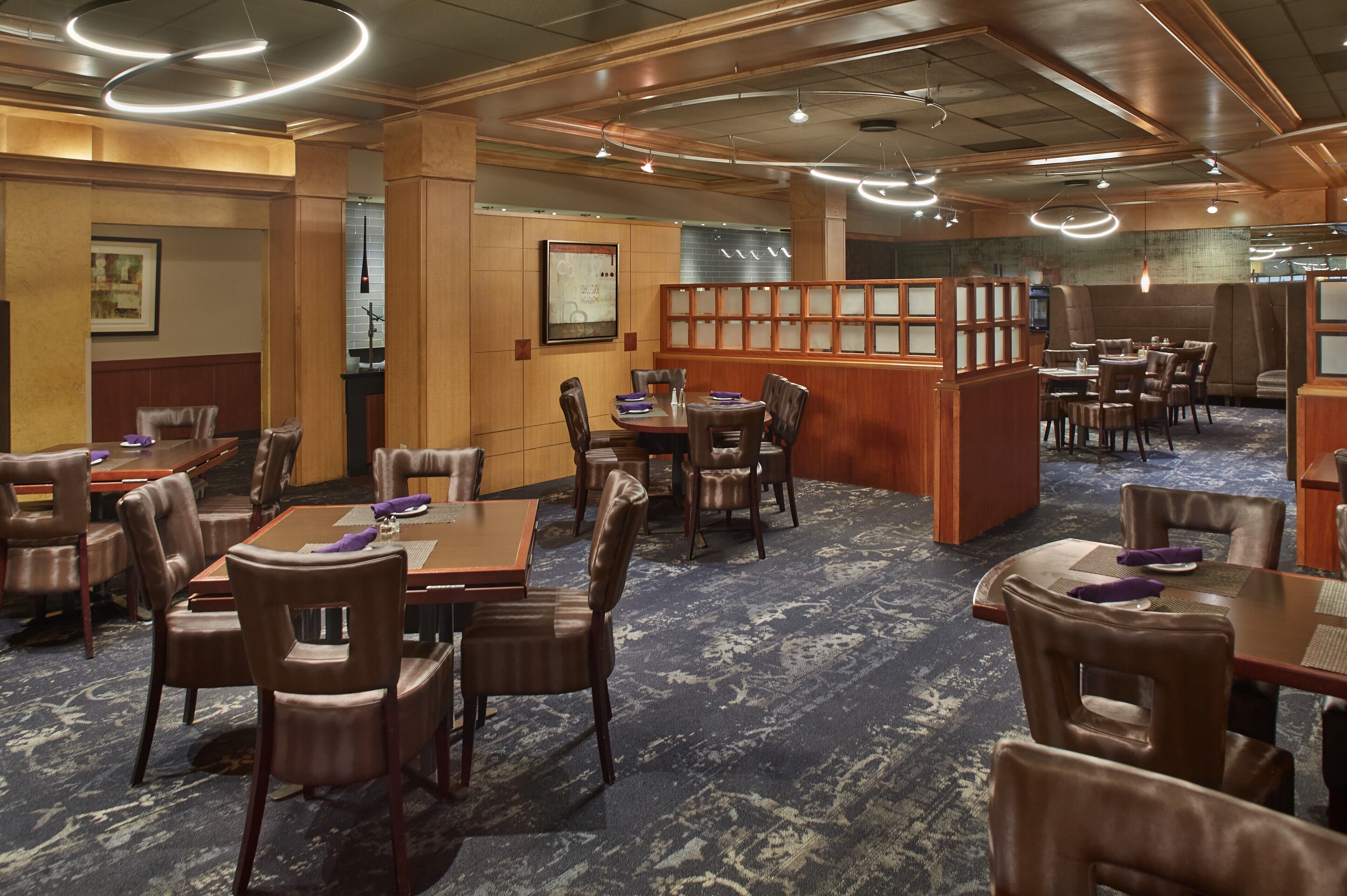 A hotel dining area with multiple tables and chairs, wooden paneling, and a patterned carpet.
