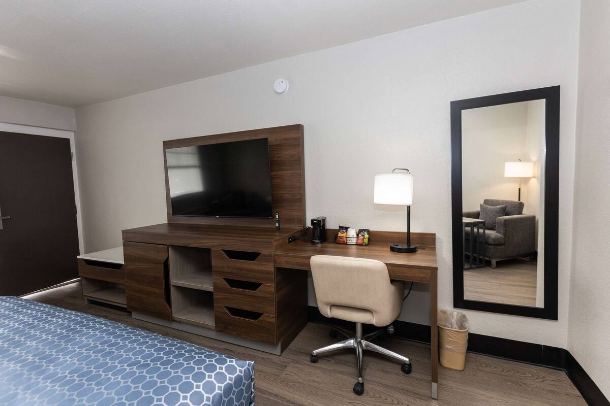 A hotel room with a wooden desk, a television, a chair, a lamp, and a mirror.
