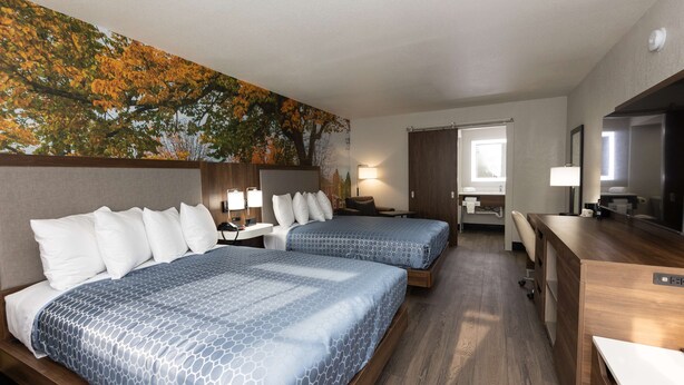Habitación de hotel con dos camas, un escritorio, una silla y un ventanal grande.