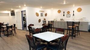 Un comedor con mesa y sillas blancas, una zona de cocina con mostrador y taburetes, y una puerta que da a otra habitación.
