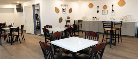 A dining area with a white table and chairs, a kitchen area with a counter and stools, and a door leading to another room.