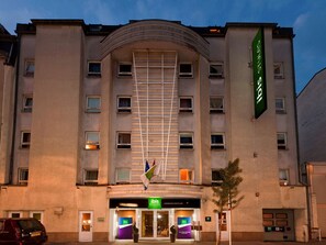 A hotel with a modern facade, multiple windows, and a prominent green flag.