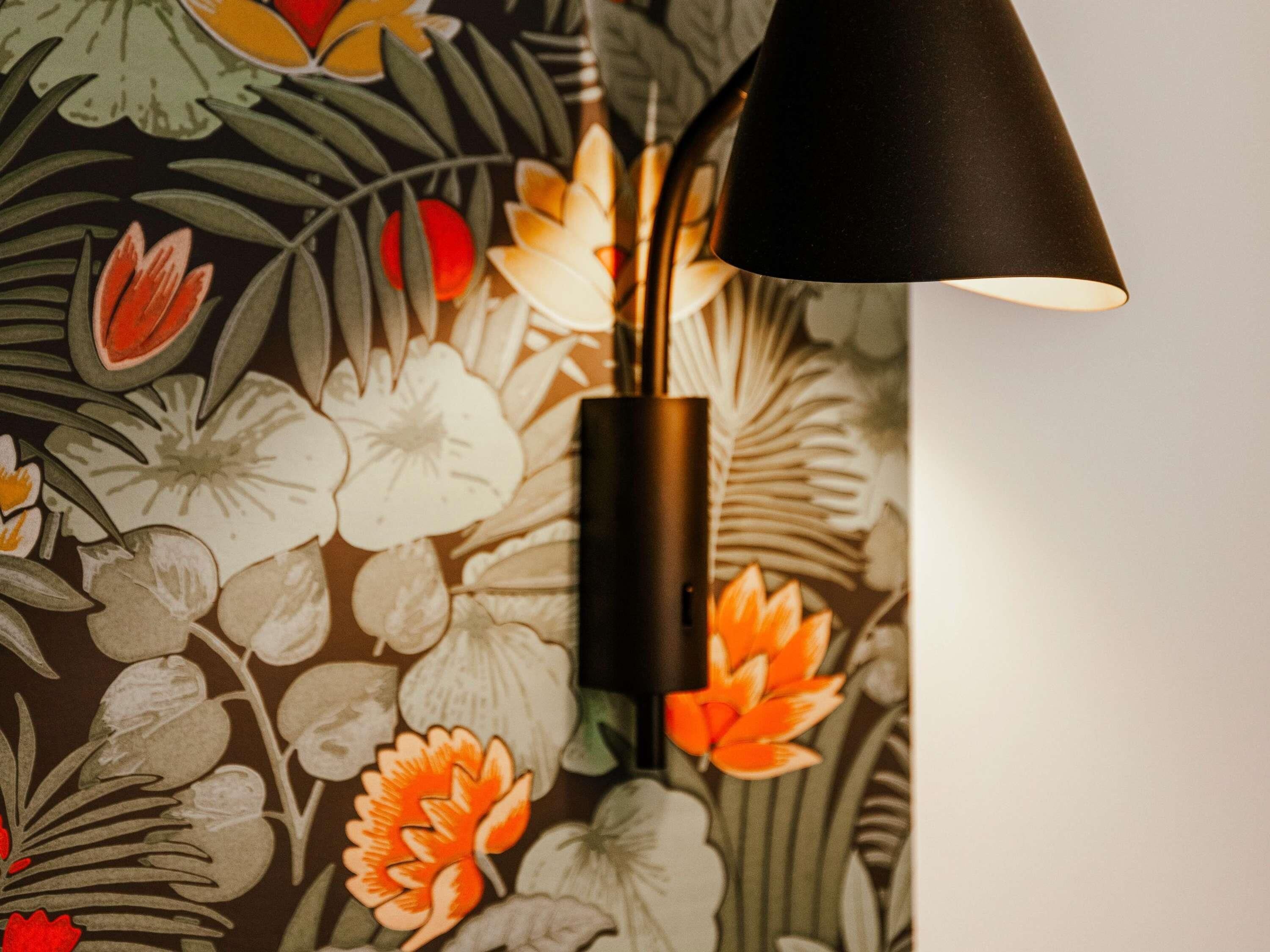 Una pared con papel tapiz floral y una lámpara colgante negra.