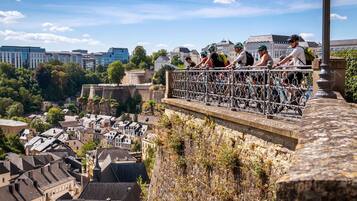 A group of cyclists on a stone bridge overlooking a city with historic buildings and a river.
