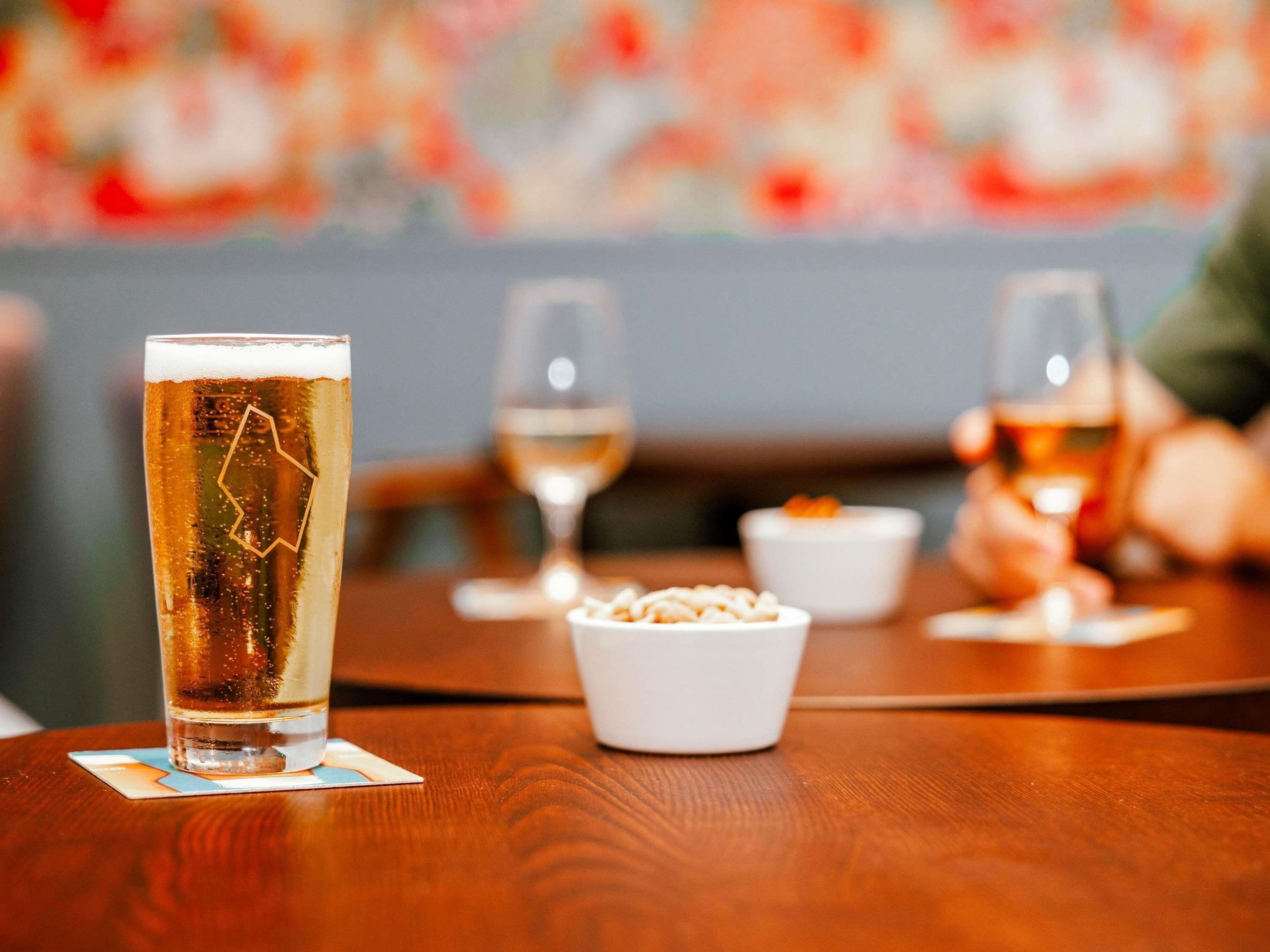 A table with a tall glass of beer, two wine glasses, and a bowl of snacks.