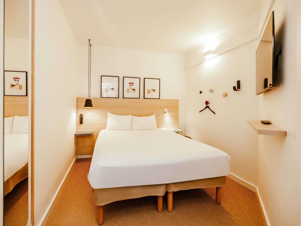 A hotel room with a large bed, a bedside table, a lamp, and framed pictures on the wall.