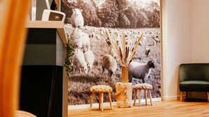 A room with a large wall mural of sheep, wooden stools, a vase with reeds, and a dark green chair. - ibis Styles Luxembourg Centre Gare (Luxembourg City)