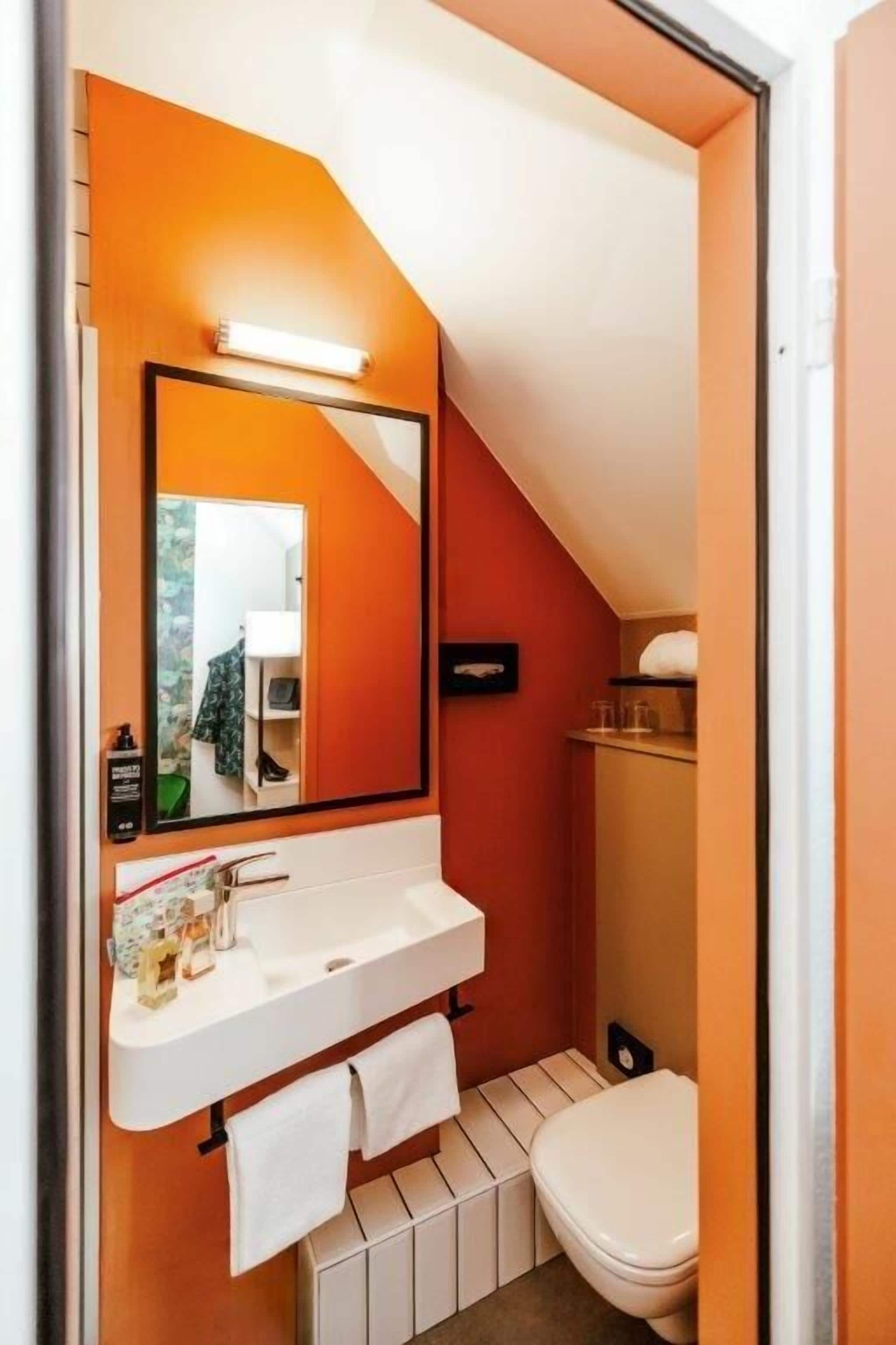 Un baño pequeño con lavamanos, espejo y retrete blancos.